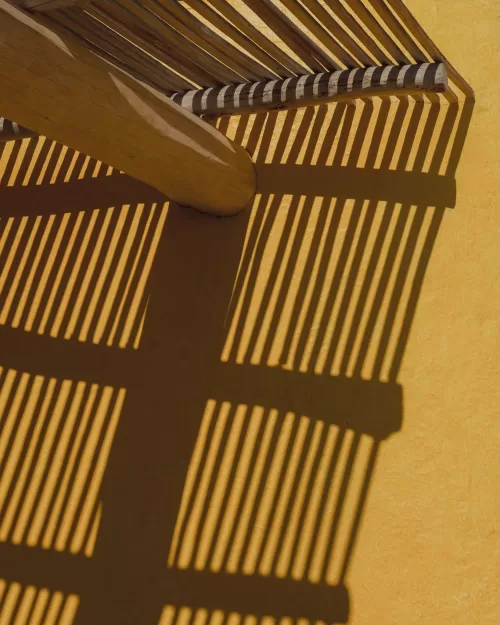 Dramatic shadows of wooden beams falling across a yellow wall in the sunlight.