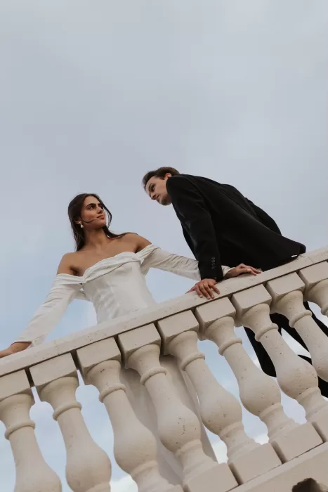 Couple leaning on the balustrade at Stone Haven, framed by classic stonework against the sky.
