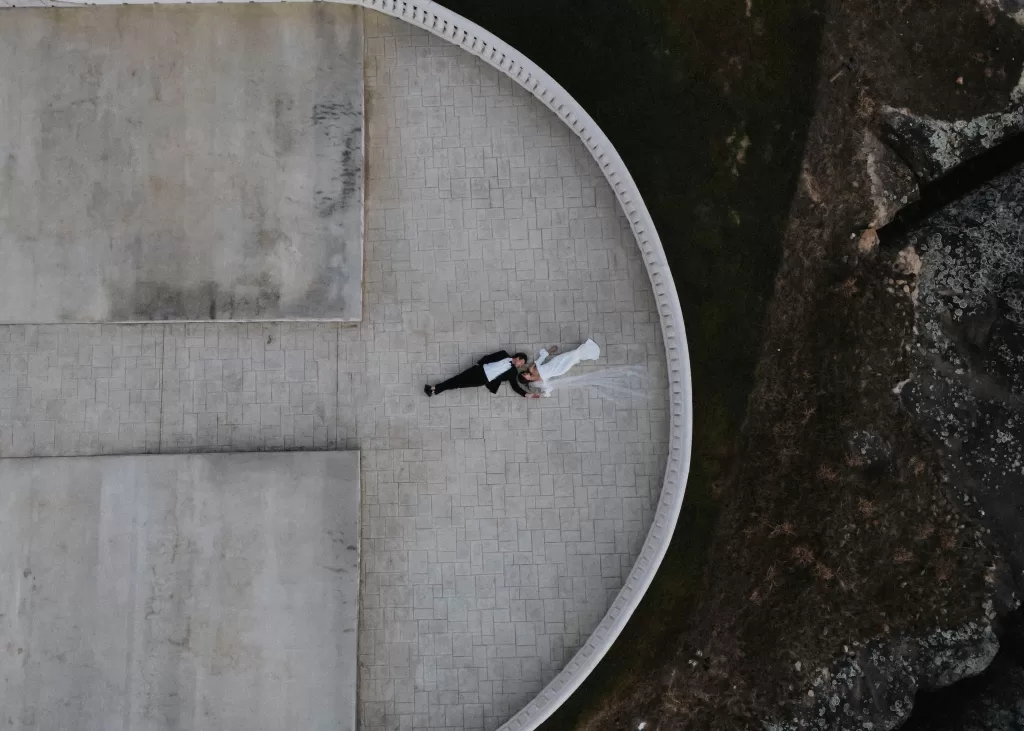 Aerial view of the bride and groom lying together on the stone terrace at Stone Haven, with her veil flowing beside them.