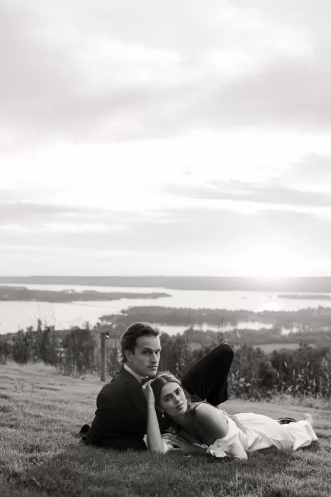 Bride resting her head on the groom’s chest as they lie on the grass overlooking the Stone Haven landscape.