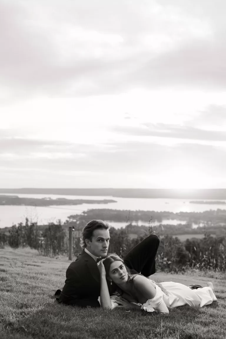 Bride resting her head on the groom’s chest as they lie on the grass overlooking the Stone Haven landscape.