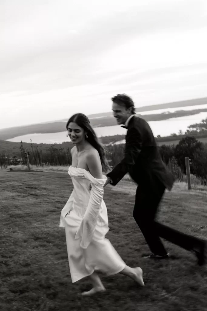 Playful black and white photo of the couple running together across the hilltop at Stone Haven.