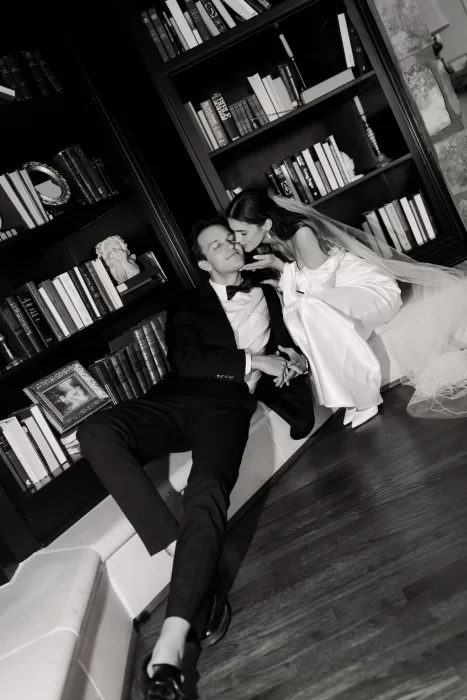 Bride kissing the groom’s cheek in Stone Haven’s library, surrounded by shelves of books.