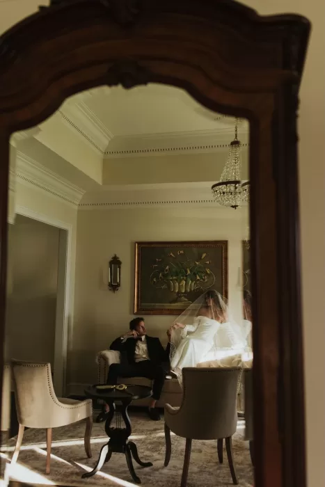 Bride and groom seen through a mirror in a vintage room at Stone Haven, creating a cinematic scene.