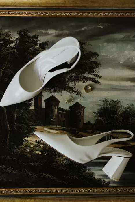 White bridal shoes and wedding rings displayed artistically on a vintage painting at Stone Haven.