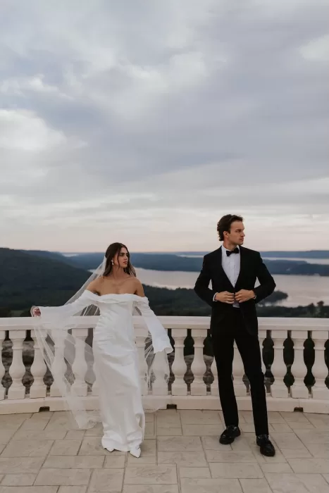 Couple standing on the Stone Haven terrace overlooking rolling hills and water at sunset.