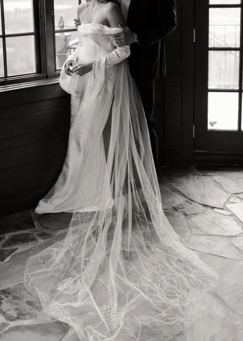 Bride in an elegant gown with a long embroidered veil, standing with the groom inside Stone Haven.