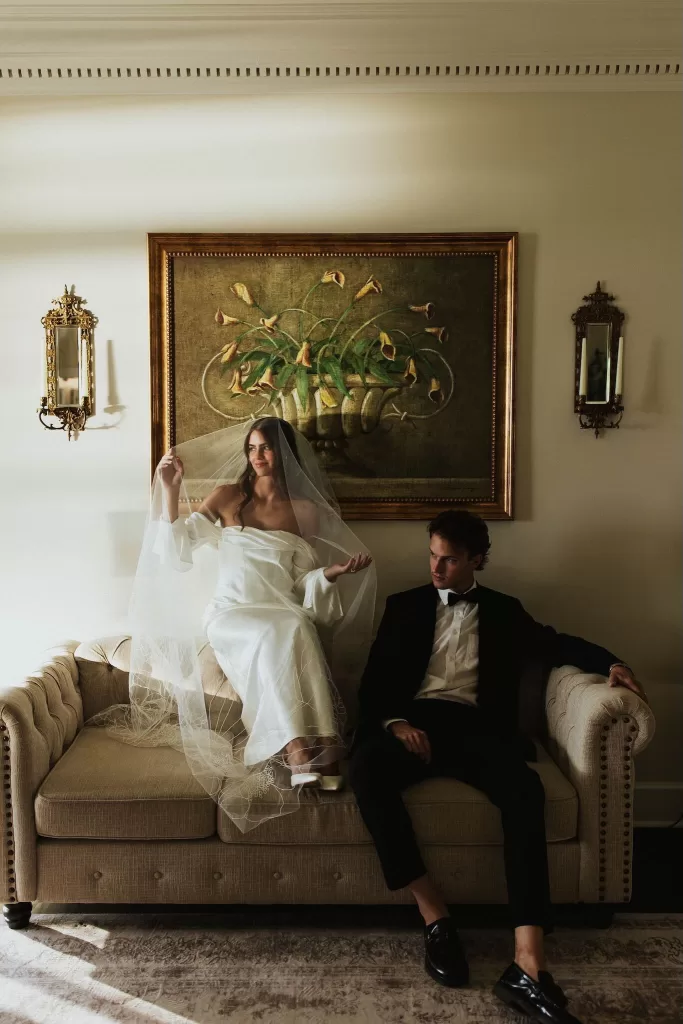 Bride sitting gracefully with veil draped over her, groom seated beside her on a sofa at Stone Haven.