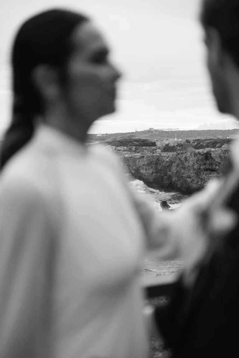 Bride and groom blurred in foreground with dramatic coastal cliffs in the distance, by Sus Pons.