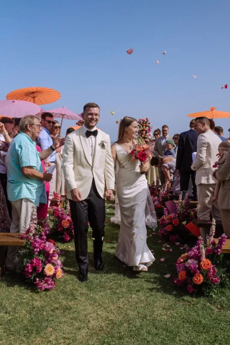 Newlyweds walk down the floral-lined aisle with guests cheering at Villa Blue Star Ibiza.