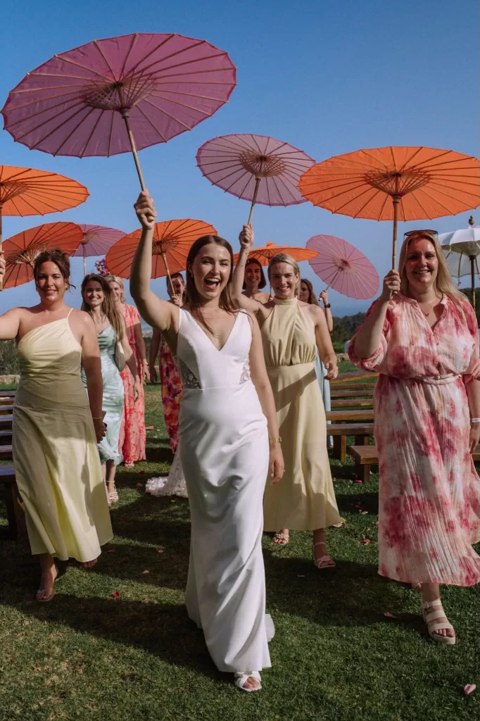 Bride walking joyfully with bridesmaids holding colorful parasols at Villa Blue Star Ibiza.