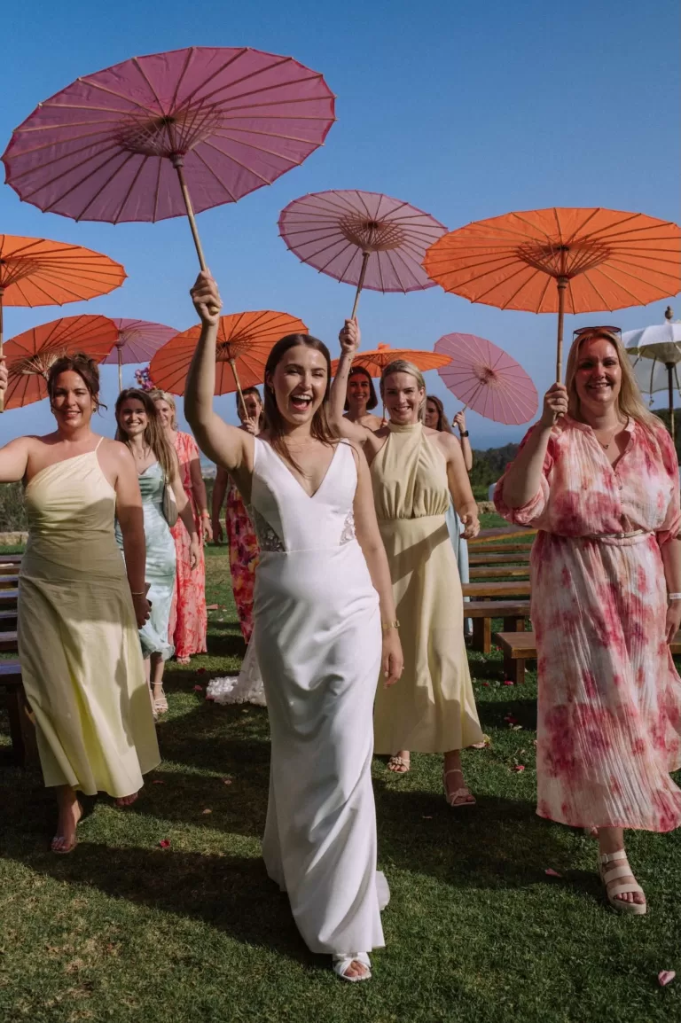 Bride walking joyfully with bridesmaids holding colorful parasols at Villa Blue Star Ibiza.