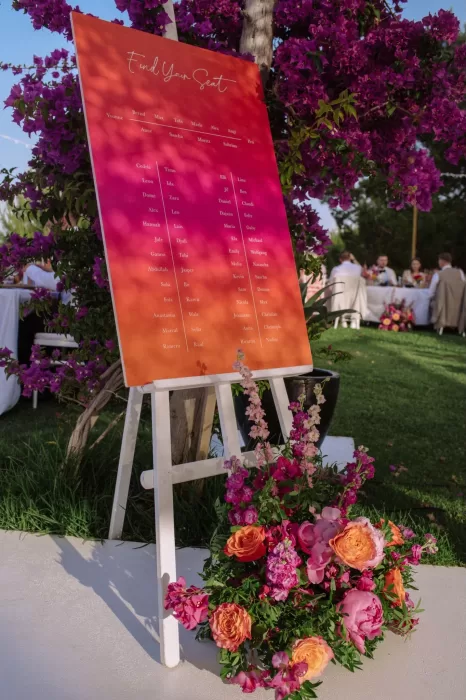 Bright pink and orange seating chart surrounded by flowers at Villa Blue Star Ibiza wedding.