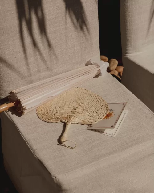 Woven fan, parasol, and ceremony program resting on a linen-covered chair.