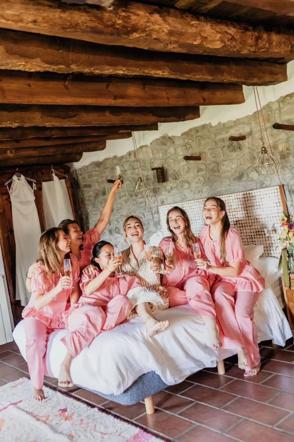 The bride and bridesmaids in matching pink pajamas celebrating with champagne in a rustic room at This Must Be The Place.