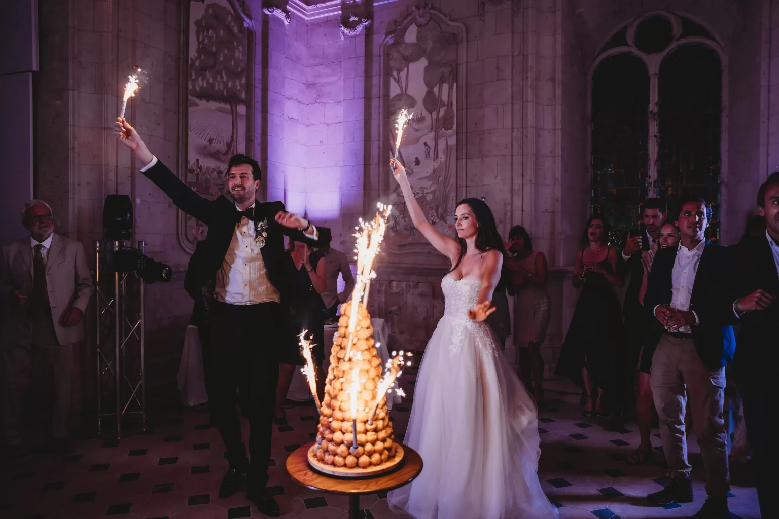 Bride and groom celebrating with sparklers beside a croquembouche wedding cake at Château de Jalesnes.