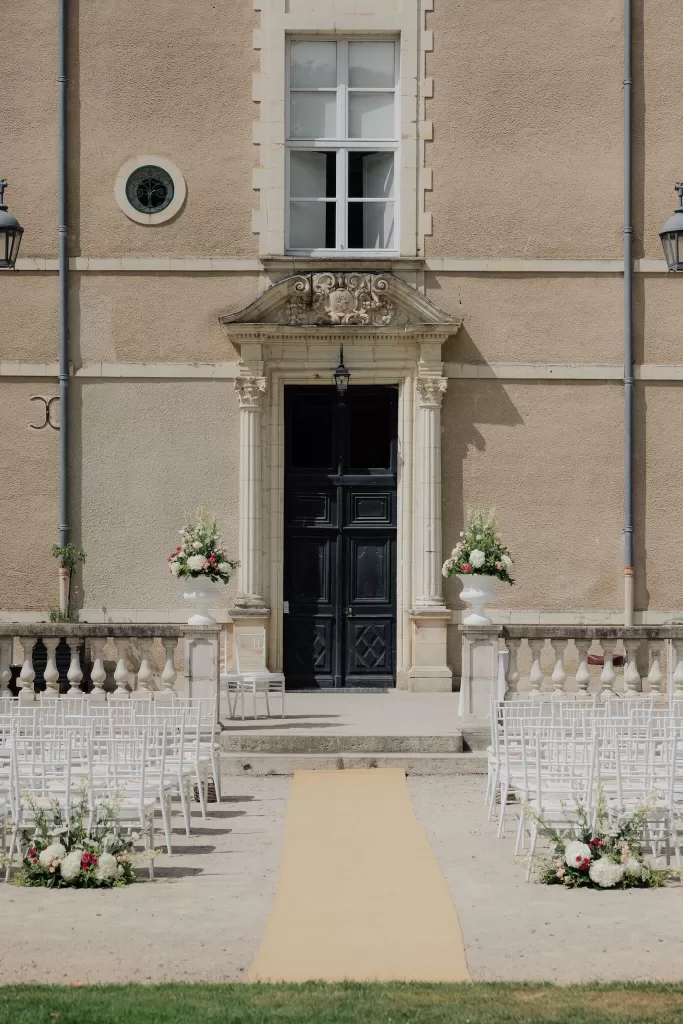 Elegant outdoor ceremony aisle leading to the grand entrance of Château de Jalesnes adorned with floral arrangements.