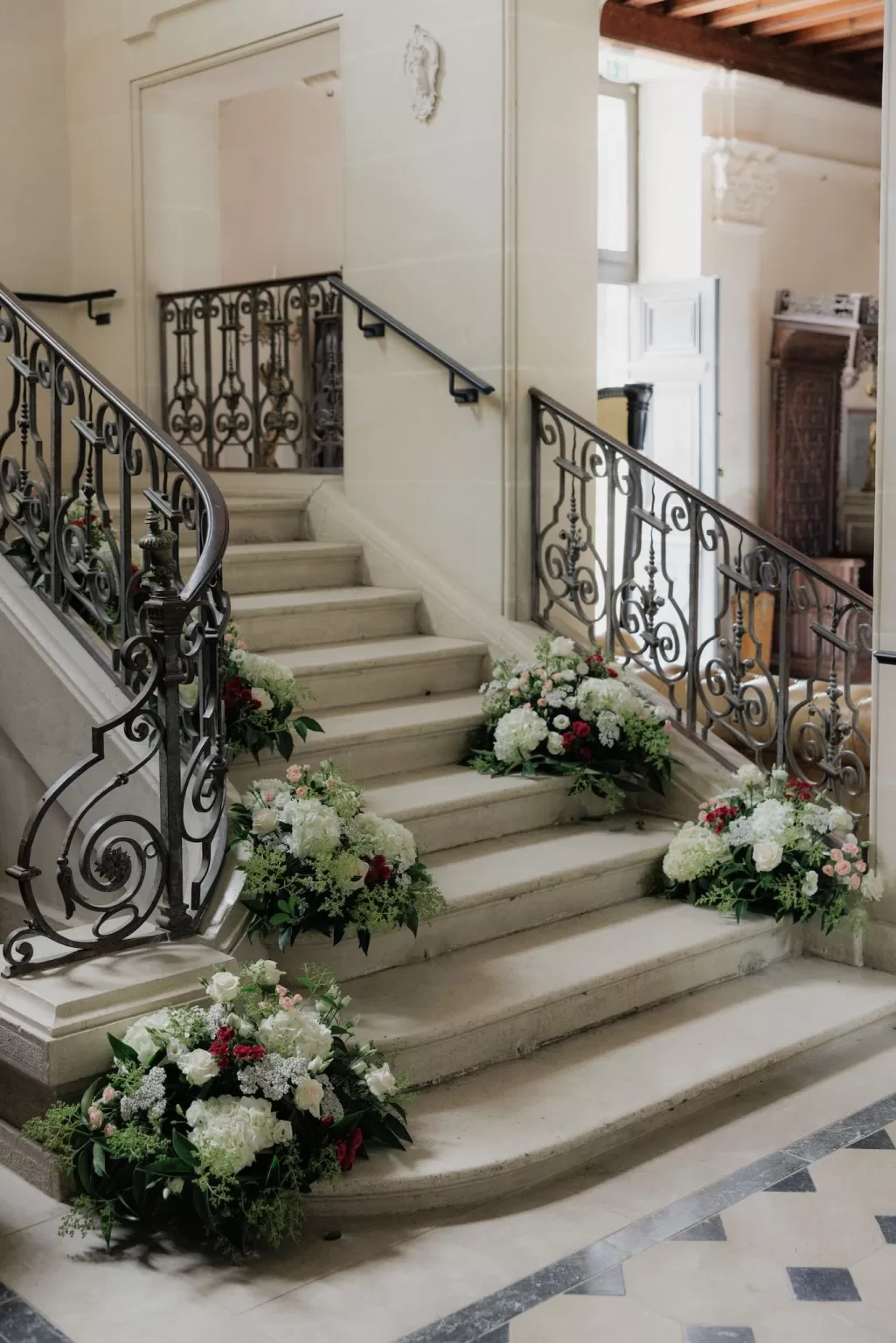 Grand staircase at Château de Jalesnes decorated with lush white and red floral arrangements for a wedding.