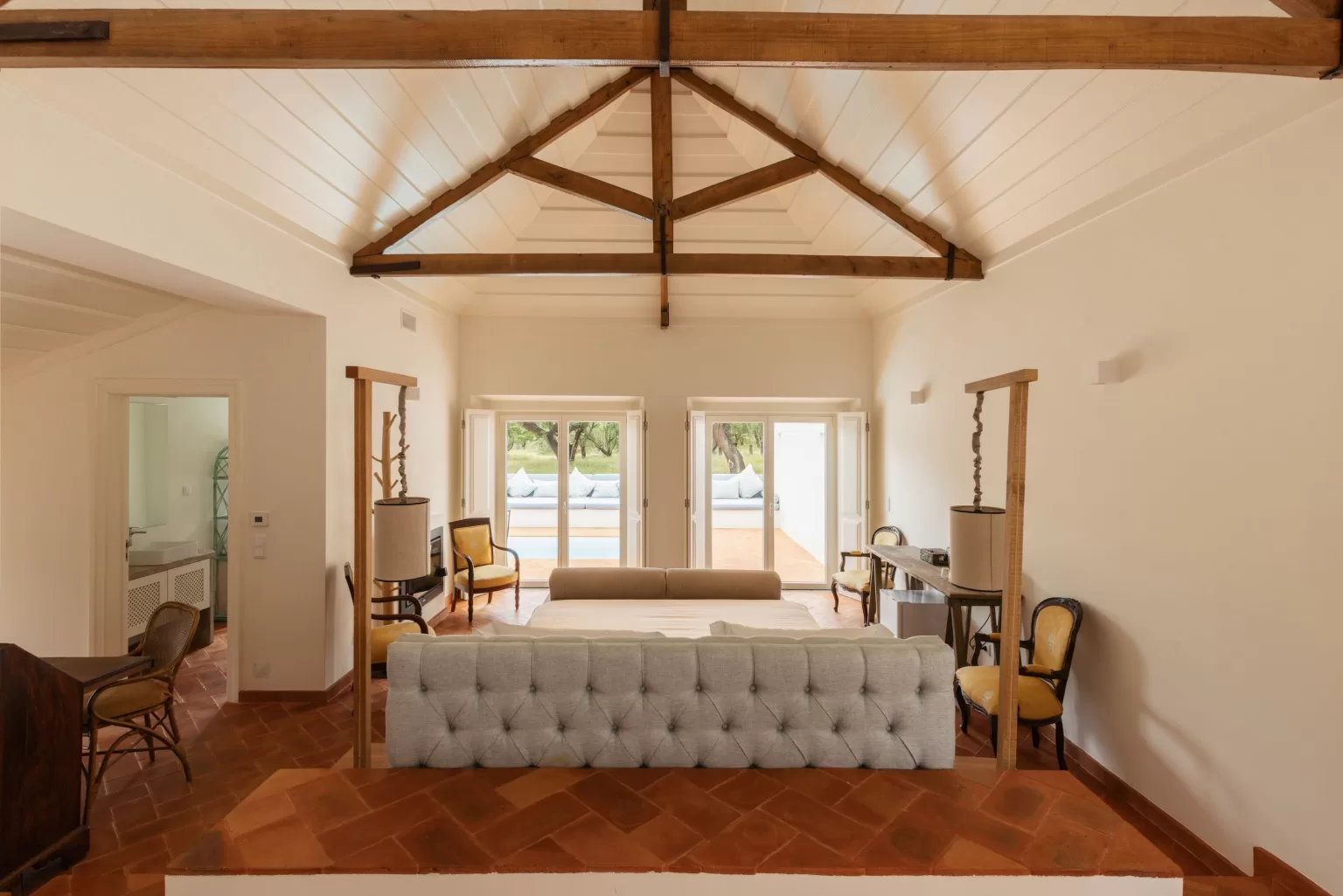Bright living room at Herdade do Peru with exposed beams, terracotta floors, and garden views through French doors.