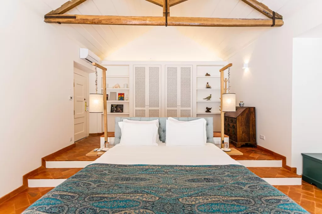 Stylish suite at Herdade do Peru featuring exposed wooden beams, terracotta floors, and crisp white bedding.