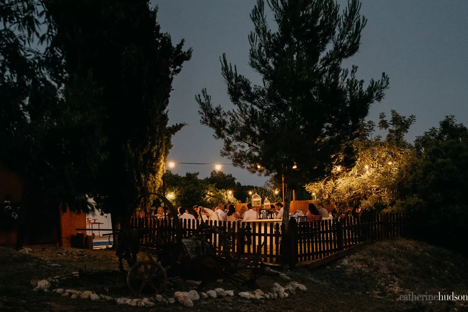 Outdoor evening dinner at Masia Can Ramonet lit by string lights, with guests dining beneath the trees in a warm, intimate setting.