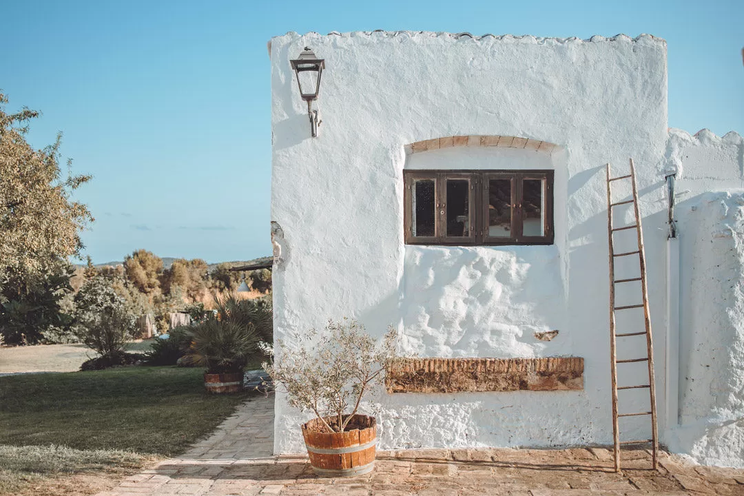 Sunlit exterior of Masia Can Ramonet with whitewashed walls, terracotta pots, and a welcoming courtyard.