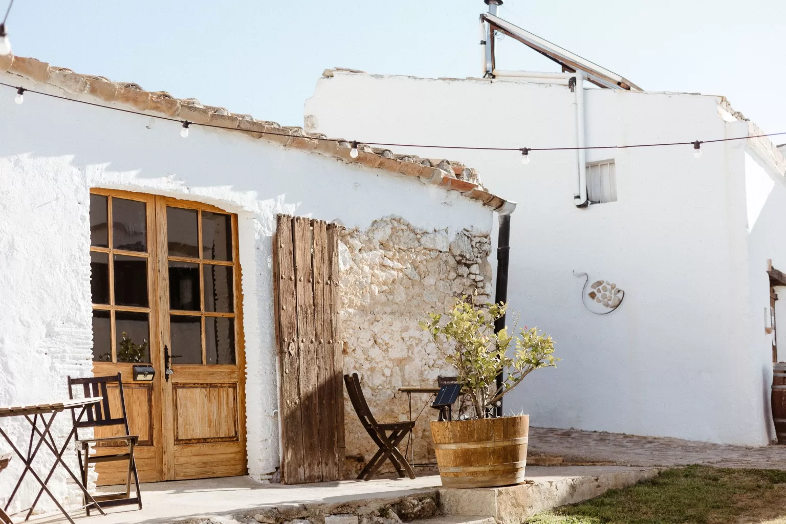 Sunlit exterior of Masia Can Ramonet with whitewashed walls, terracotta pots, and a welcoming courtyard.