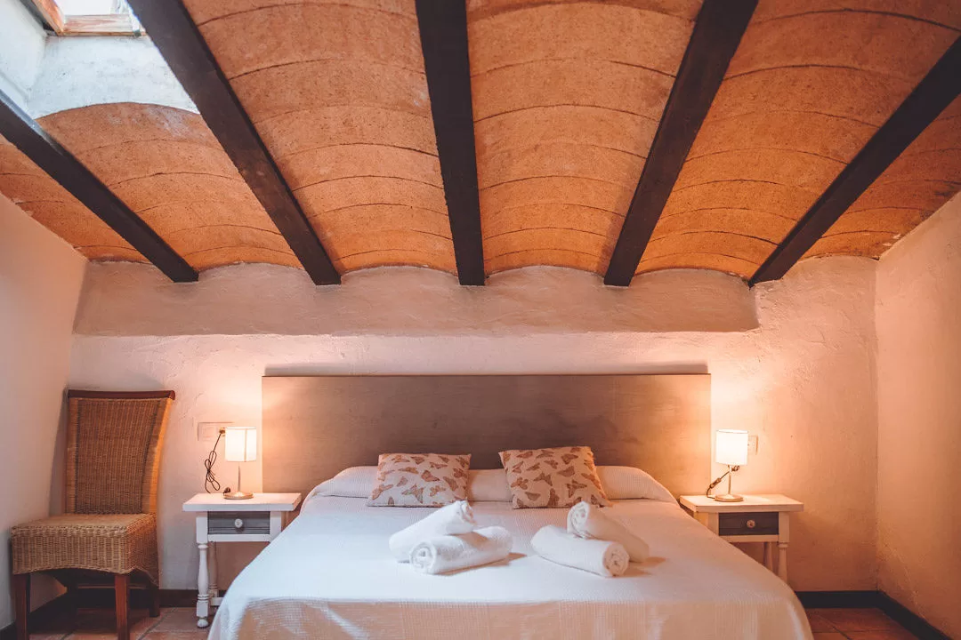 Cosy guest bedroom at Masia Can Ramonet with wooden beams and warm ambient lighting.
