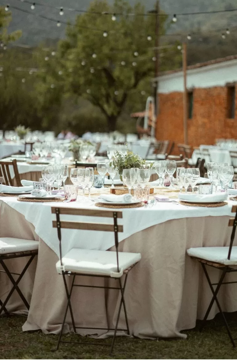 Elegant outdoor wedding table setup at Masia Can Ramonet with linen tablecloths and glassware under string lights.