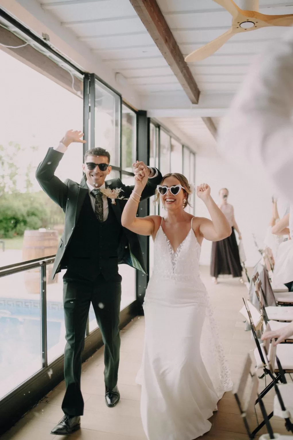 Newlyweds celebrating joyfully at Masia Can Ramonet with heart-shaped sunglasses and bright natural light.