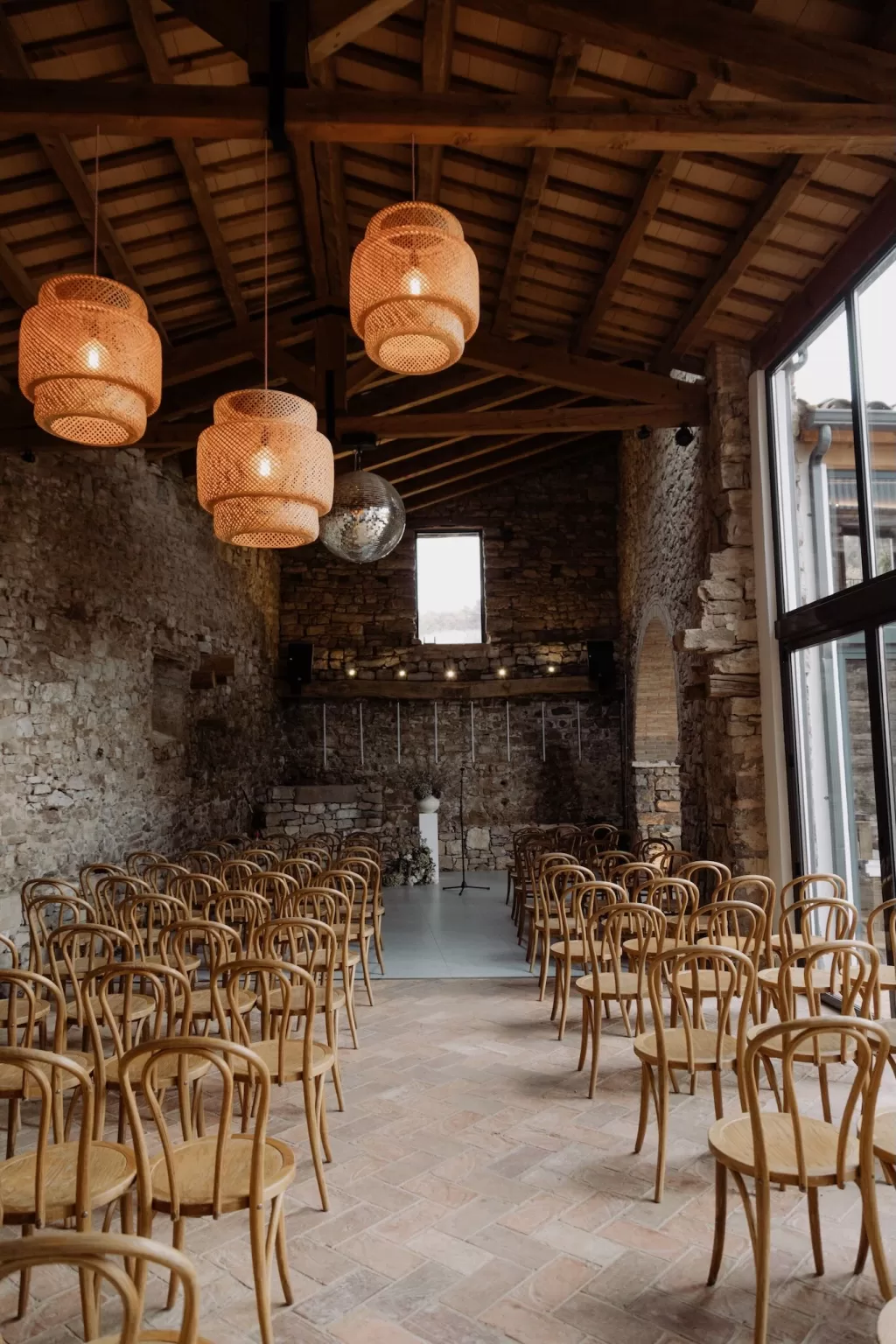 Ceremony setup in the stone barn at This Must Be The Place with wooden chairs and warm hanging lights.
