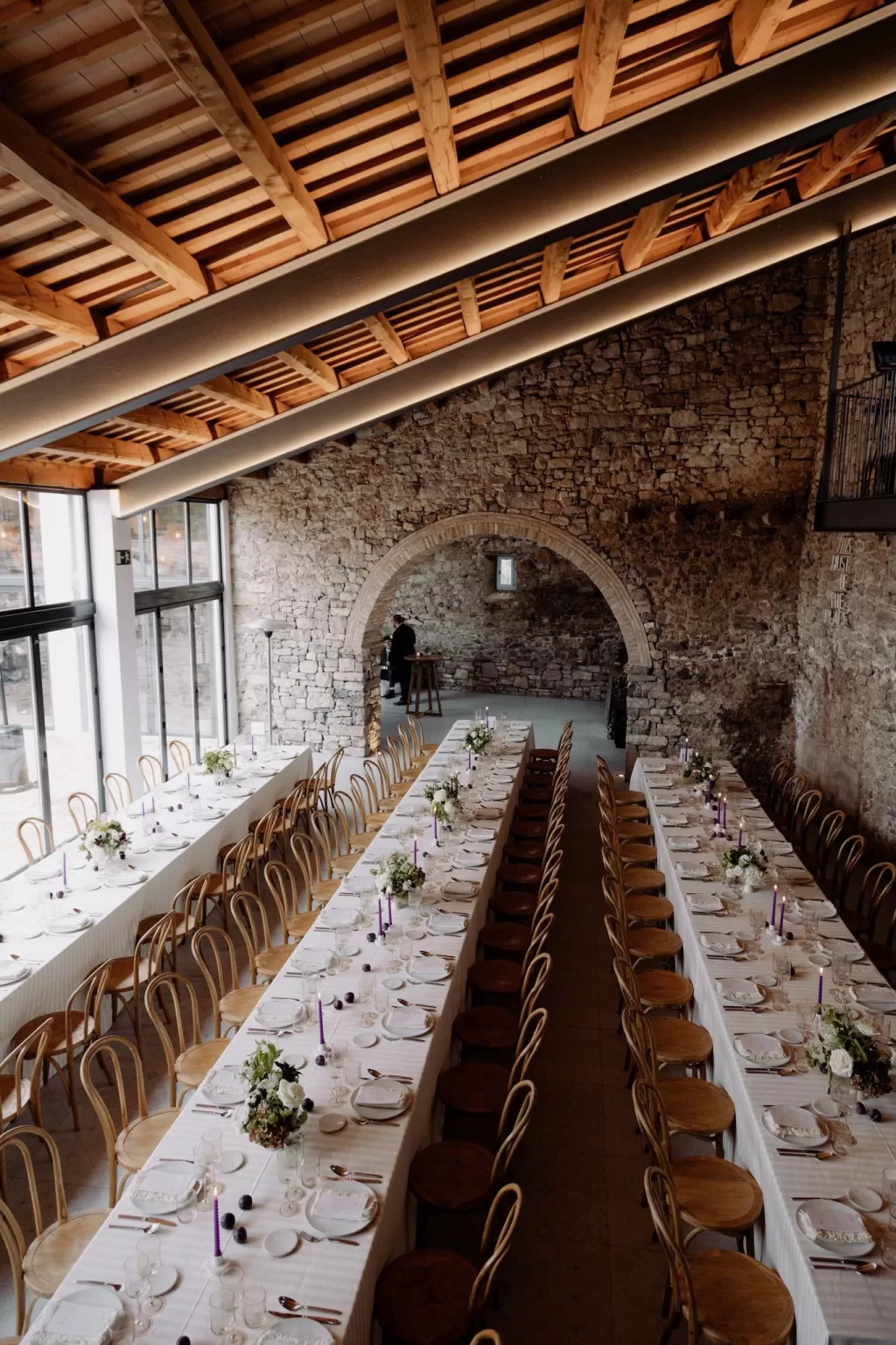 Elegant reception tables lined with flowers and lilac candles inside the stone-walled hall at This Must Be The Place