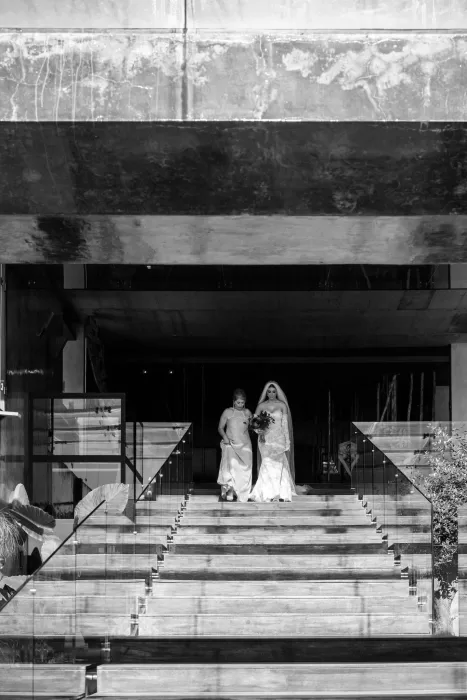The bride descends the modern glass-lined staircase at Areias do Seixo, sunlight highlighting the architectural concrete textures.
