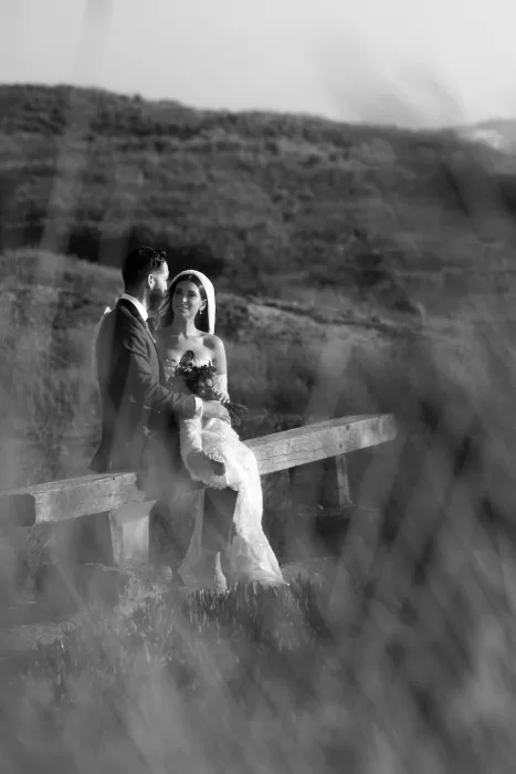 Intimate black-and-white portrait of the couple sitting together on a wooden bench in the dunes near Areias do Seixo.