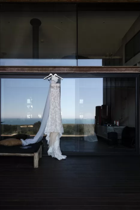 Wedding dress hanging beside the large glass windows of Areias do Seixo, reflecting ocean views and natural light.