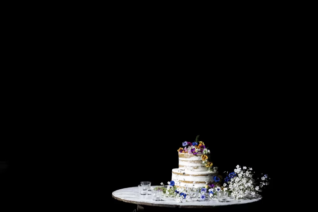 A rustic naked wedding cake decorated with colourful flowers at Areias do Seixo, styled on a simple round table.