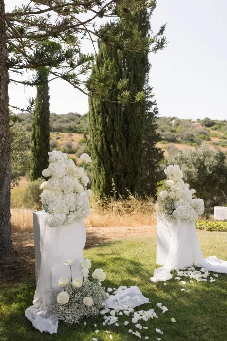 White floral ceremony arrangements at Casa Arte set on a grassy hilltop surrounded by tall cypress trees and soft golden landscape.