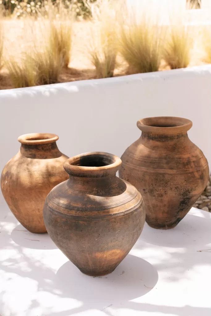 Rustic clay urns displayed on a sunlit terrace at Casa Arte, surrounded by natural grasses and soft shadows.