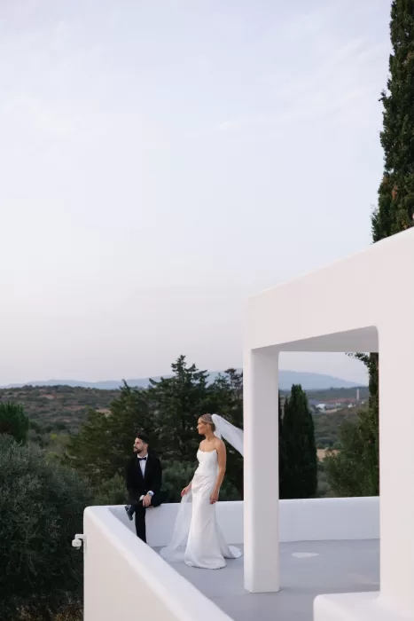 Bride and groom standing on the modern white terrace at Casa Arte, overlooking the rolling hills during the soft early evening light.