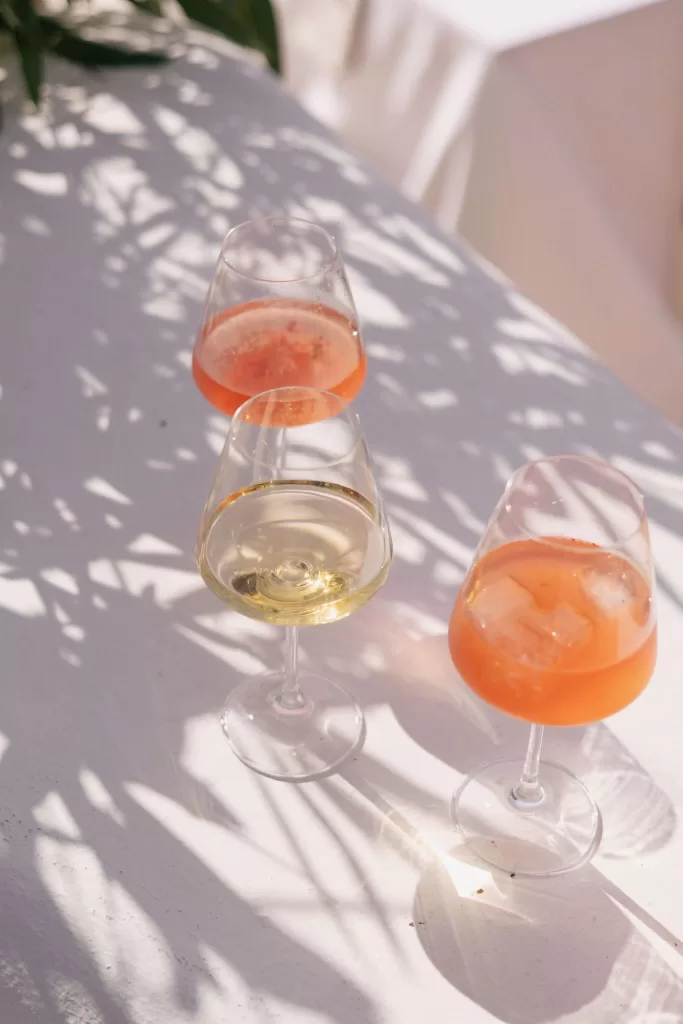 Three glasses of rosé spritz and white wine catching the sunlight on a white terrace at Casa Arte.