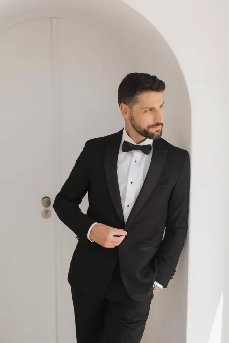 Groom standing in a white arched doorway at Casa Arte, adjusting his suit in natural morning light.