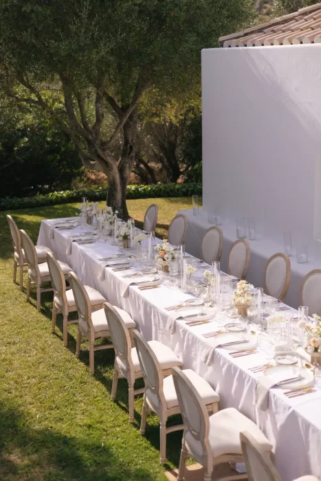 Refined outdoor reception table at Casa Arte shaded by an olive tree, styled with white florals and neutral-toned chairs.