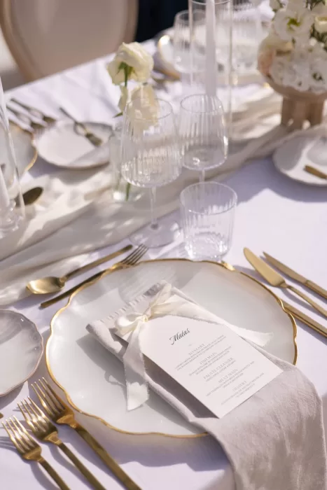 Elegant table setting at Casa Arte featuring gold-rimmed plates, clear glassware, and soft white florals in the afternoon light.