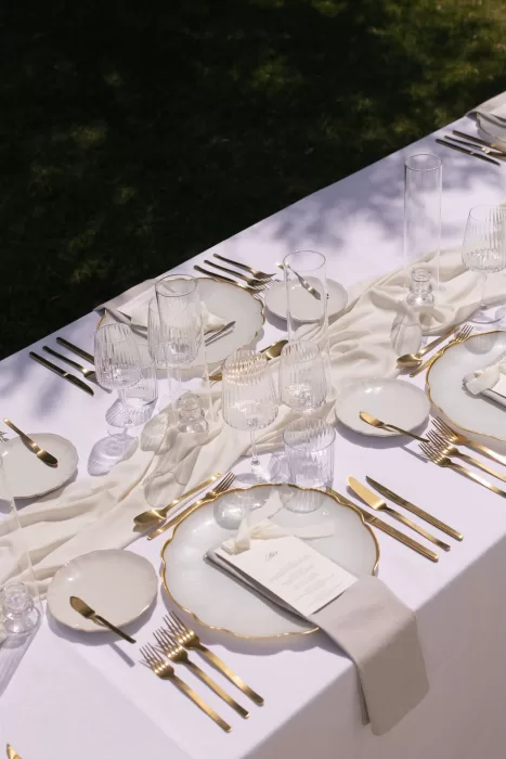 Elegant minimal table setting at Casa Arte featuring gold flatware, clear glassware, and soft ivory linens.