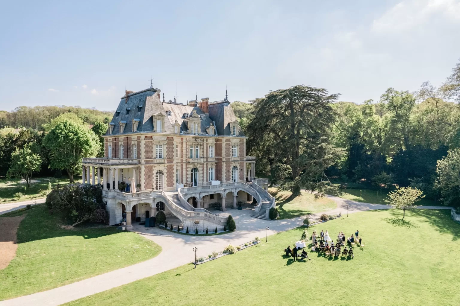 A sunny aerial view of Château Bouffémont with an intimate outdoor ceremony set on the expansive lawn surrounded by lush greenery.