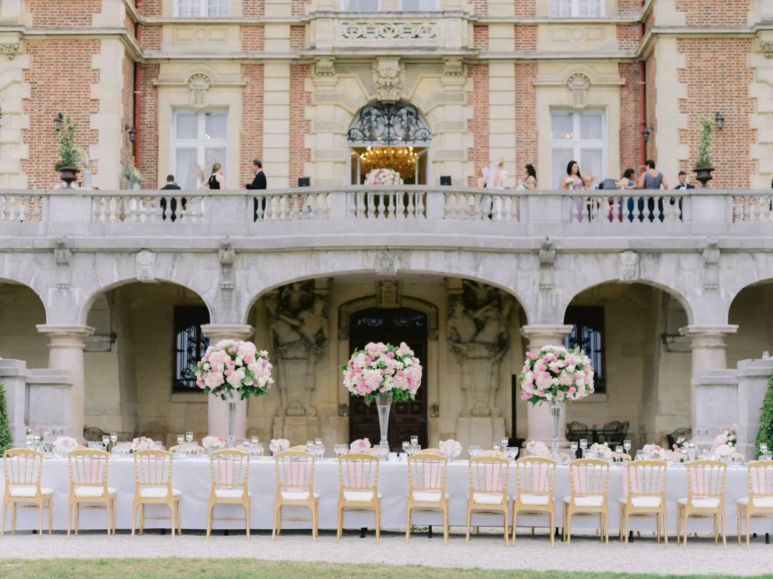 Long outdoor reception table at Château Bouffémont styled with tall pink floral arrangements in front of the château’s lower terrace.