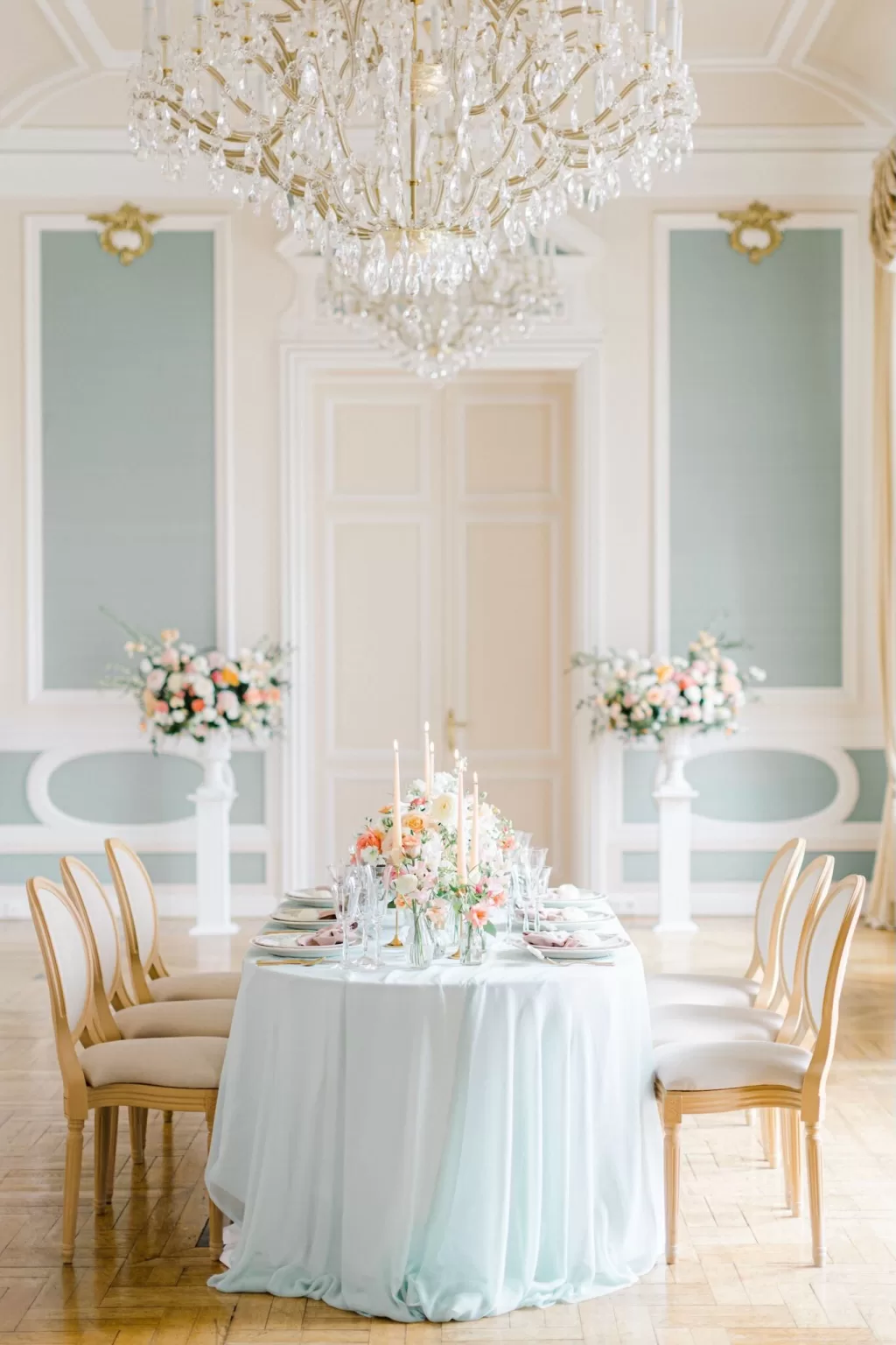 Round pastel-themed reception table set beneath sparkling chandeliers inside Château Bouffémont’s elegant dining hall.
