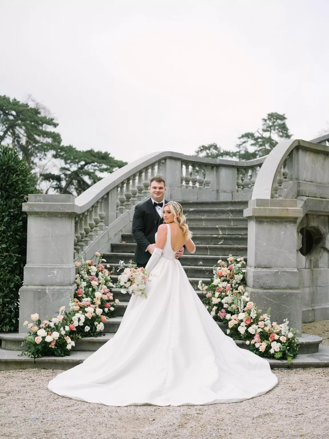 Newlyweds posing on Château Bouffémont’s sweeping stone staircase adorned with pastel floral clusters.