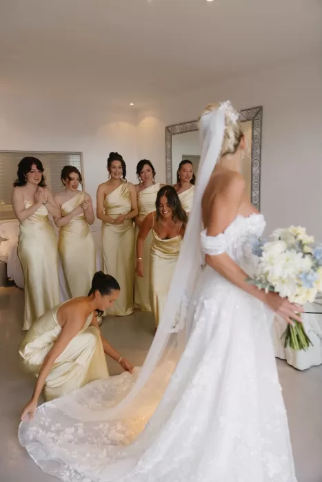 Bride surrounded by bridesmaids in champagne gowns as they admire her dress at Hacienda Na Xamena.