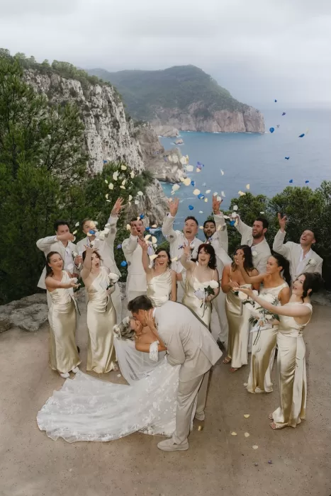 Wedding party throwing petals in the air as the couple kisses against the coastal cliffs of Hacienda Na Xamena.